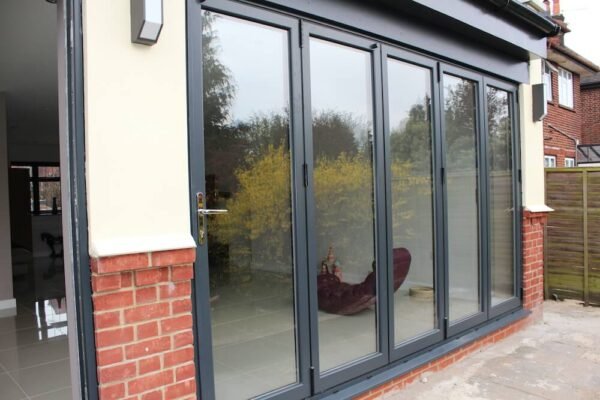 Modern grey aluminium bifold doors fully opened, connecting indoor and outdoor living spaces.